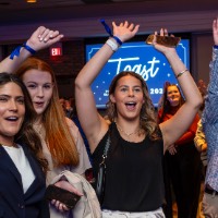 People with their hands raised in the air to grab an Alumni shirt that is being thrown out to crowd.